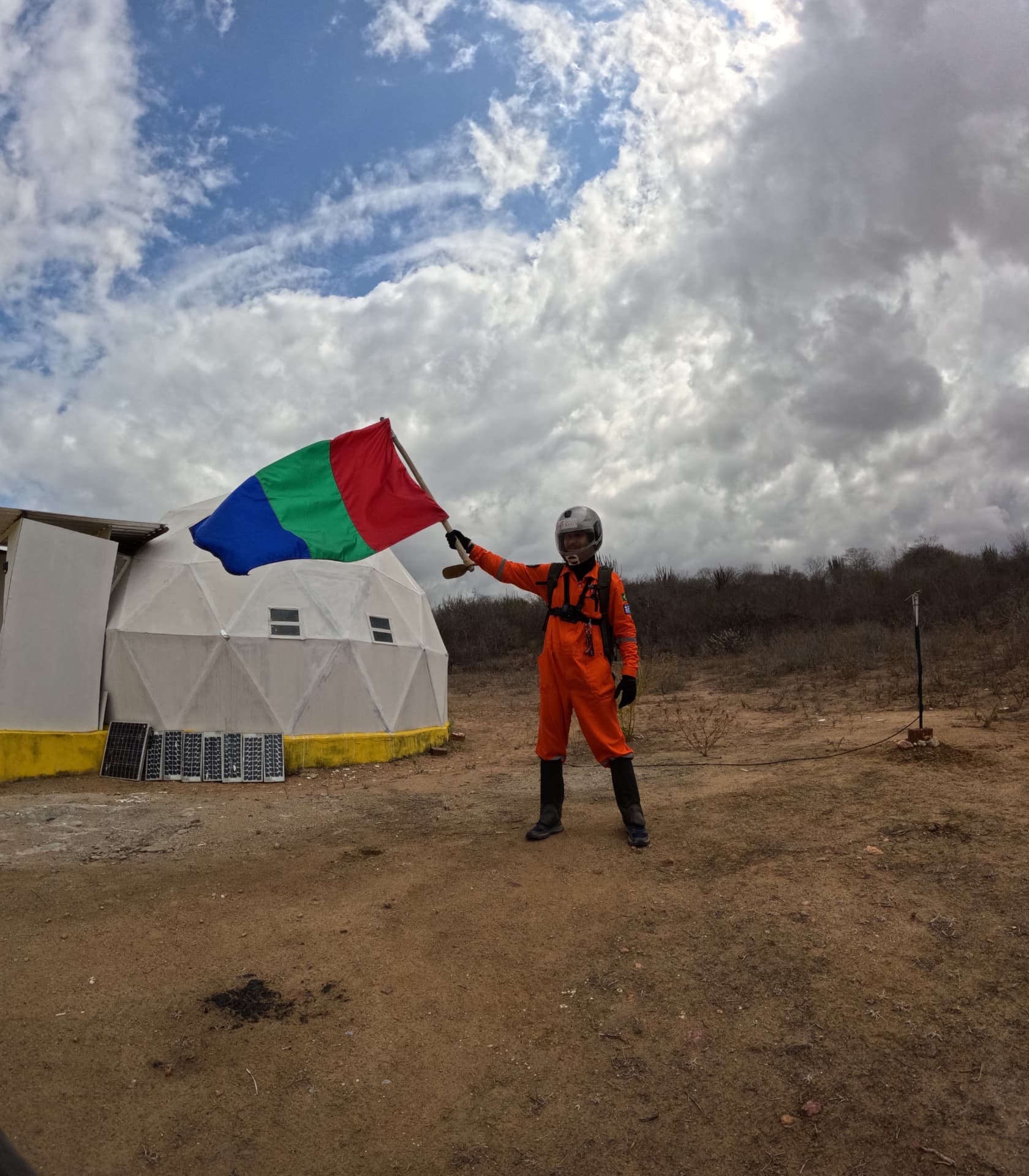 Analog astronaut raising the Mars flag next to the habitat dome at HABITAT MARTE